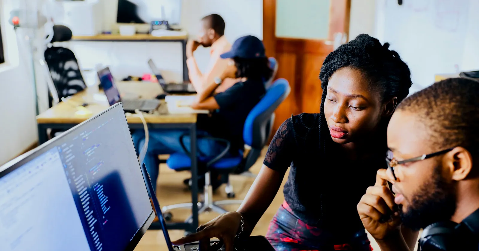 Two developers reviewing code together on a monitor and laptop
