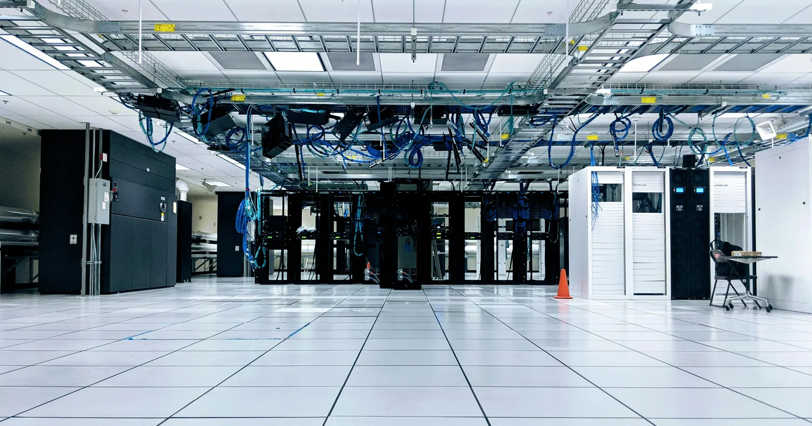 A brightly lit data center floor with rows of server cabinets and network cables in overhead trays