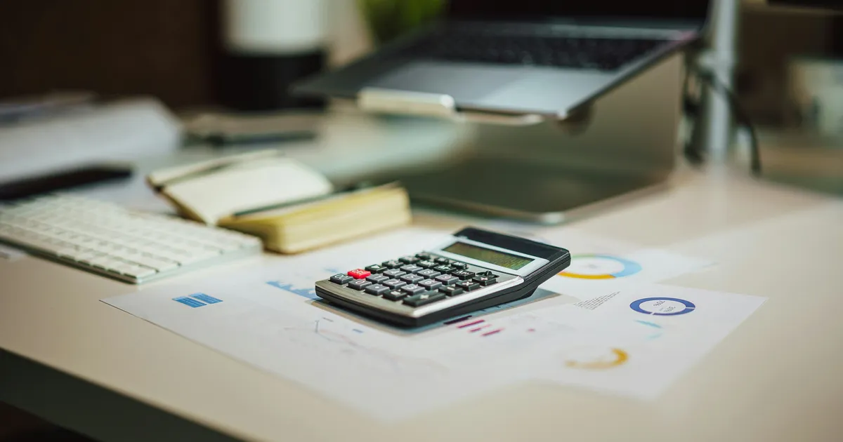 A calculator next to a laptop and printed charts on a desk