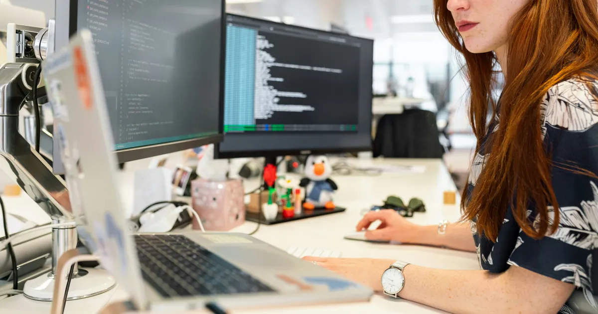 A software engineer writing code at a desk with two monitors